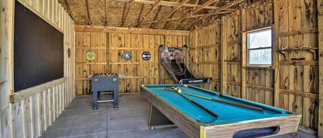 A wooden room with a pool table, a foosball table, and two dartboards on the walls.
