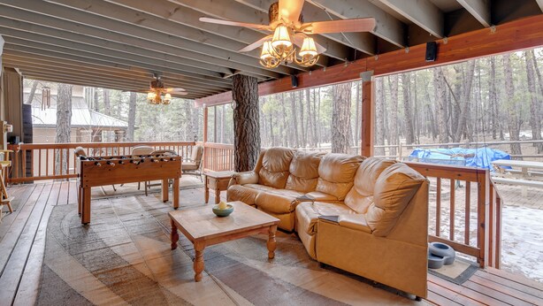 A covered outdoor area with a wooden deck, a leather sofa, a wooden coffee table, and a foosball table. - Near Hiking & Golfing: Munds Park Cabin w/ Deck! (Munds Park)
