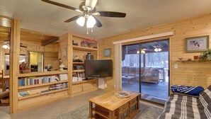 A cozy living room with wooden walls, a ceiling fan, a flat-screen TV, a coffee table, and a sofa. - Near Hiking & Golfing: Munds Park Cabin w/ Deck! (Munds Park)