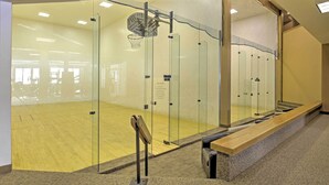 A gym with glass walls, a wooden floor, and a basketball hoop. - Luxe Fraser Condo: Community Pool and Hot Tub Open (Fraser)