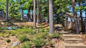 Ett bostadsområde med en trätrappa som leder upp till ett hus med ett grönt tak, omgivet av höga tallar.