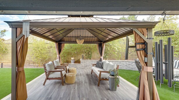 Een overdekt terras met buitenmeubilair, een hanglamp en uitzicht op een tuin.