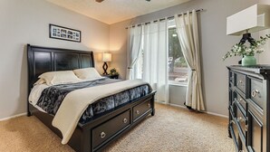Een slaapkamer met een bed, een plafondventilator, een dressoir en een raam met gordijnen.