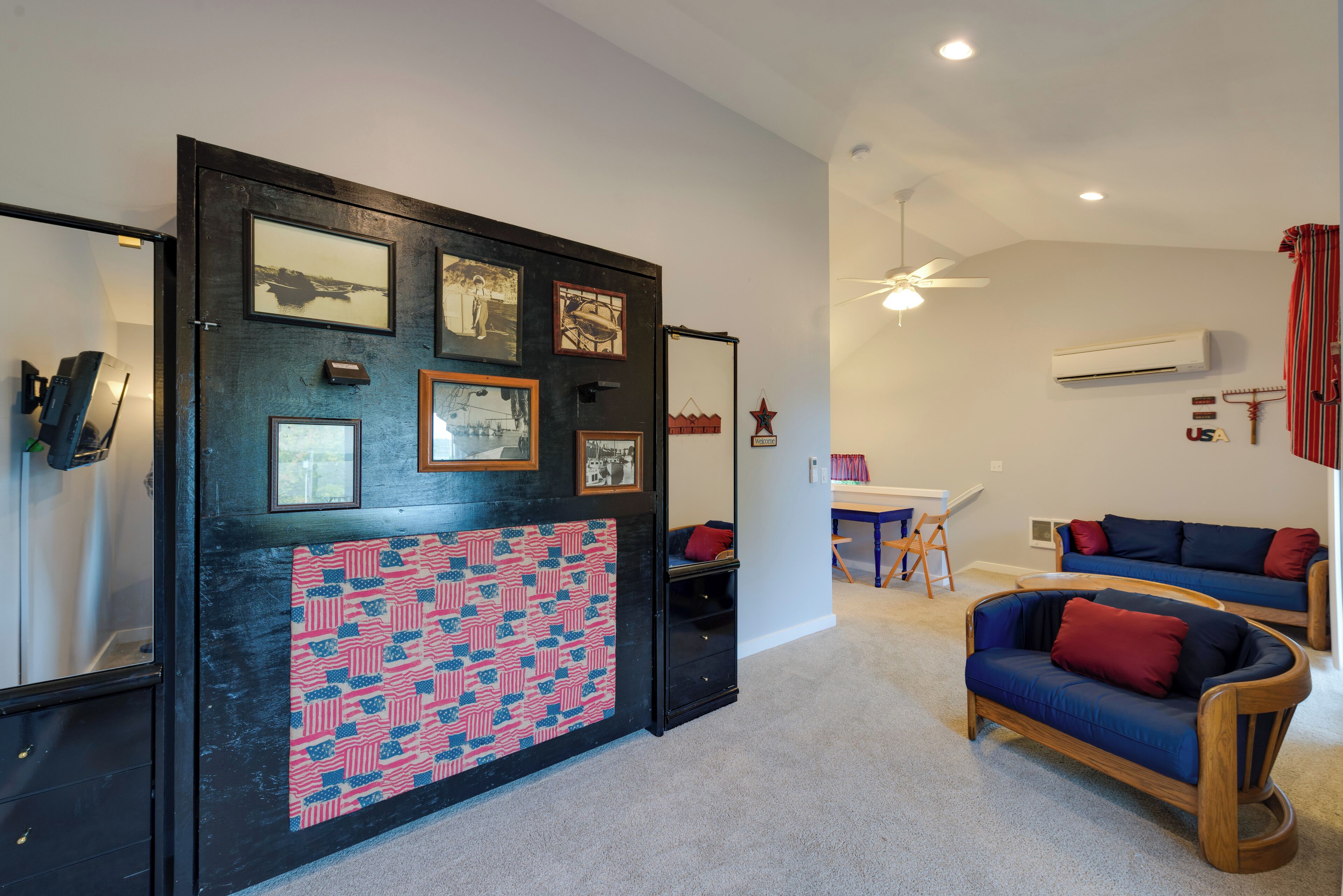 A room with a black-framed door, a ceiling fan, a white air conditioner, and two blue sofas with red cushions.