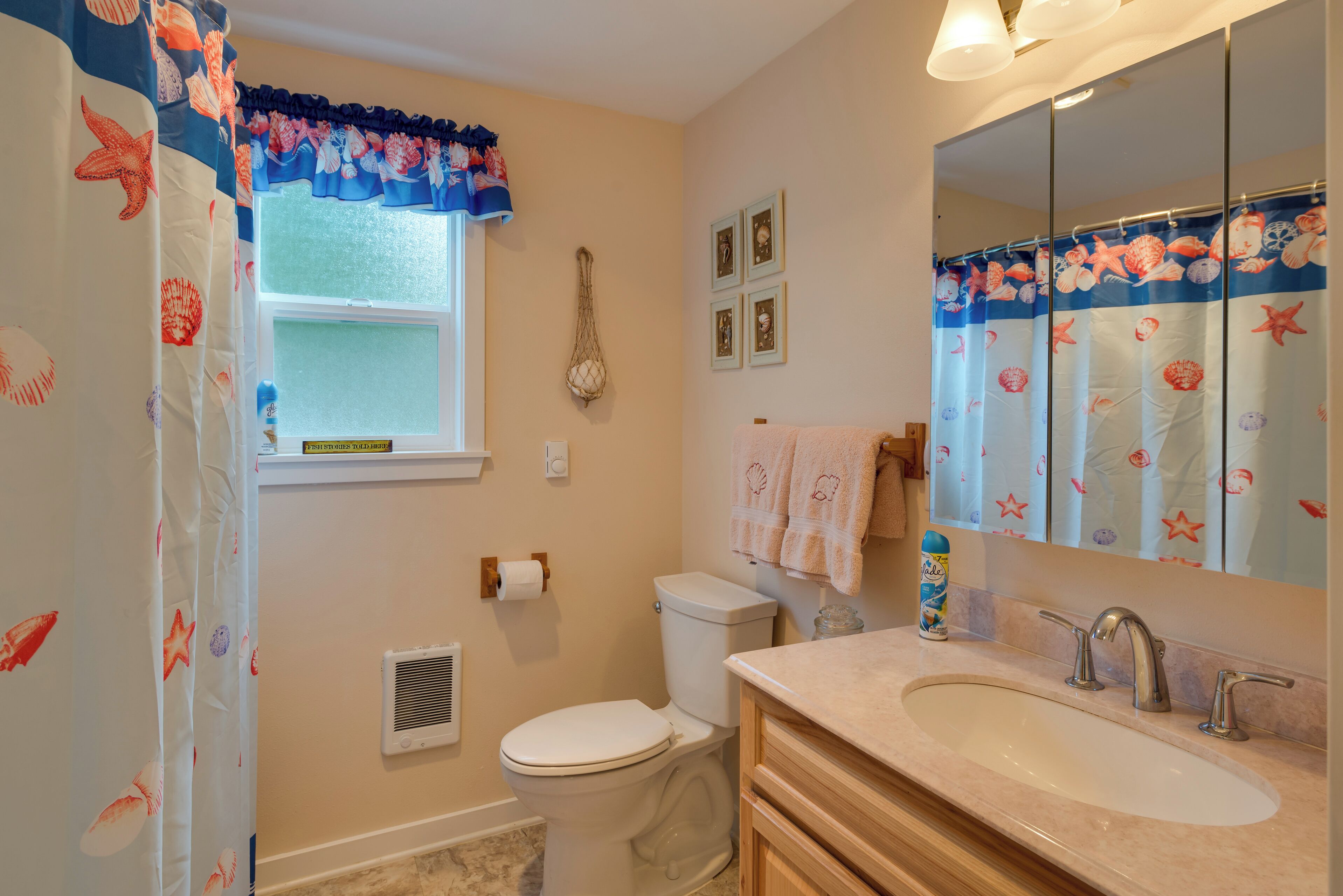 A bathroom with a toilet, sink, and shower curtain with a sea theme.
