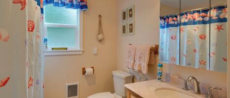 A bathroom with a toilet, sink, and shower curtain with a sea theme.