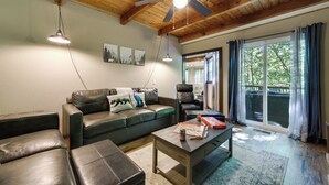 A living room with a leather couch, a coffee table, and a ceiling fan. There are framed pictures on the wall and a window with curtains.