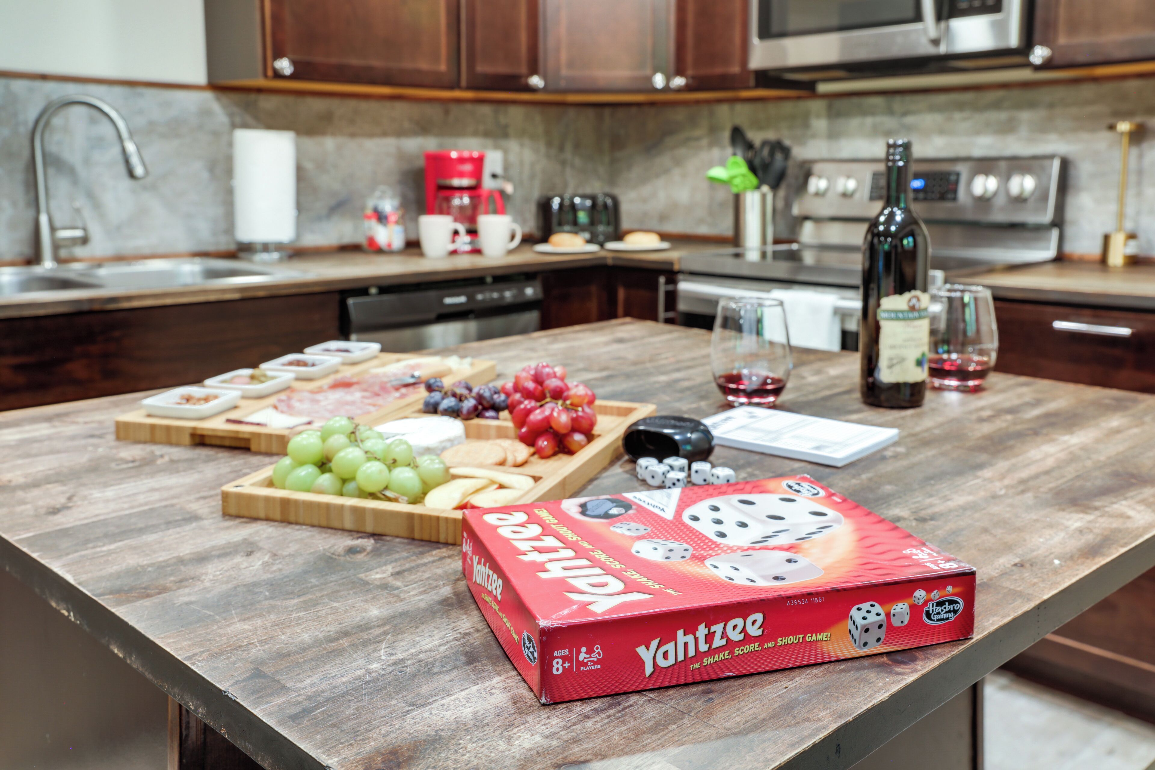 A kitchen counter with a Yahtzee game box, a bottle of wine, and various snacks.