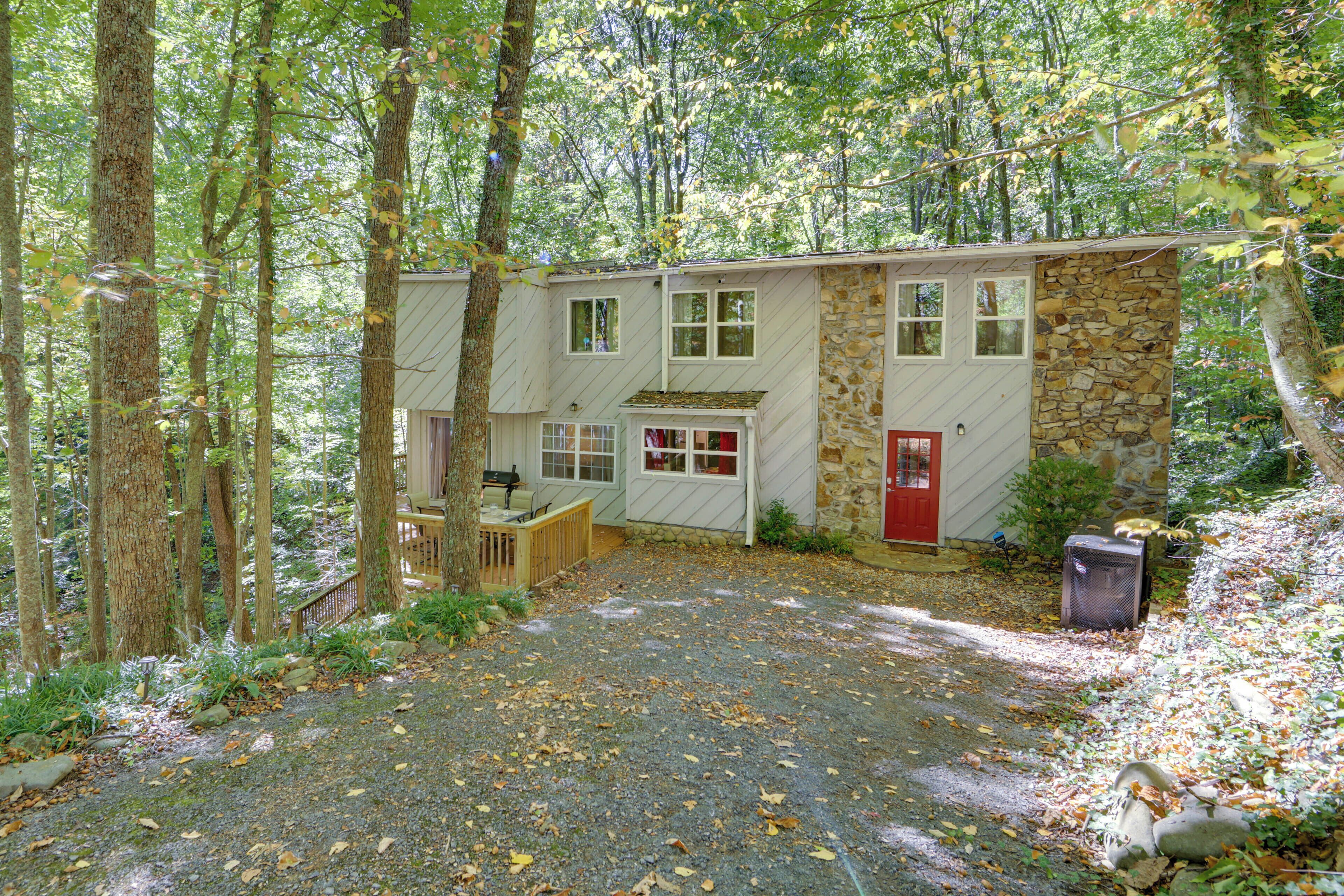 A cabin with a stone exterior, a red door, and a gravel driveway surrounded by trees.