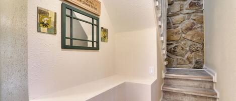 A staircase with a stone wall and a white wall with a wooden sign and two small framed pictures.