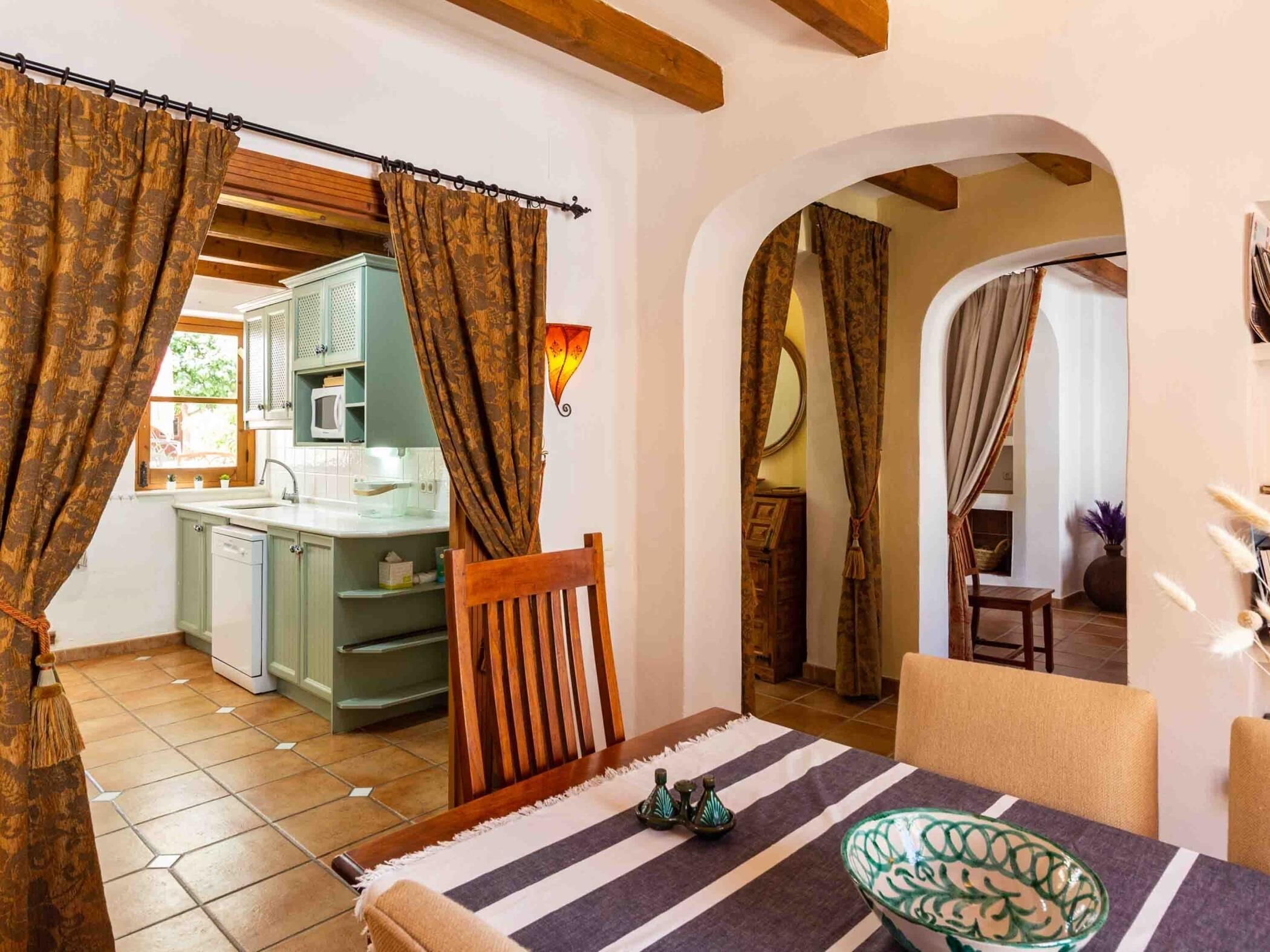 Un coin repas accueillant, avec une table dressée pour deux personnes, une chaise en bois et un bol décoratif. Un arc donne accès à une cuisine équipée d’un four à micro-ondes et de placards.