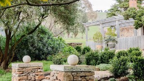 A garden with stone structures, a pergola, and various shrubs. - Restored Luxury Historic Glenroy Homestead (Mansfield)