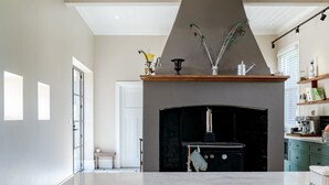 A modern kitchen with a central island, wooden stools, pendant lighting, and a black stove. - Restored Luxury Historic Glenroy Homestead (Mansfield)