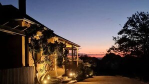 A house at dusk with a driveway leading to the entrance, surrounded by trees and a wooden fence. - Restored Luxury Historic Glenroy Homestead (Mansfield)