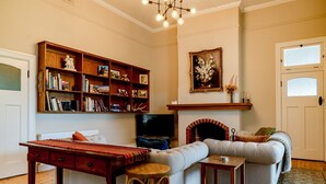 A cozy living room with a fireplace, a bookshelf, a sofa, and a television. - Restored Luxury Historic Glenroy Homestead (Mansfield)