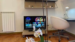A modern office space with a television displaying a film channel, a white office chair, and a potted orchid plant. - Home Roman Center Neptune (Nettuno)