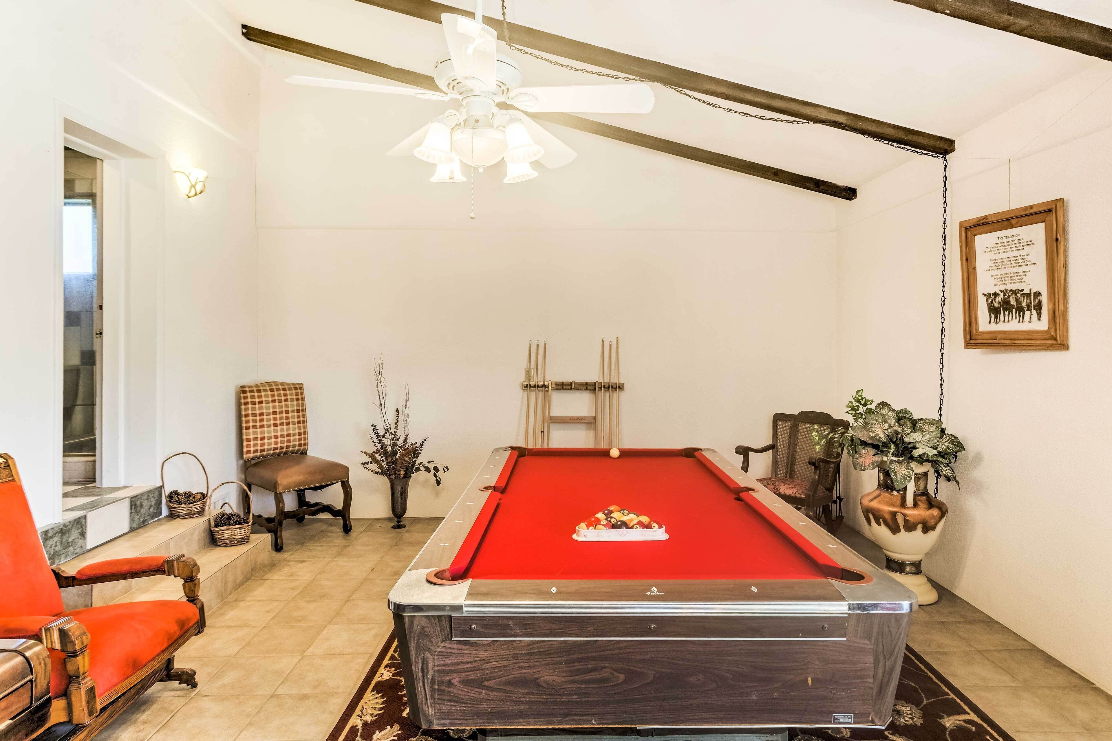 A pool table with a red felt surface, a ceiling fan, and a framed certificate on the wall.