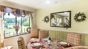 A dining area with a round table set for four, plaid chairs, a mirror, and two wreaths on the wall.