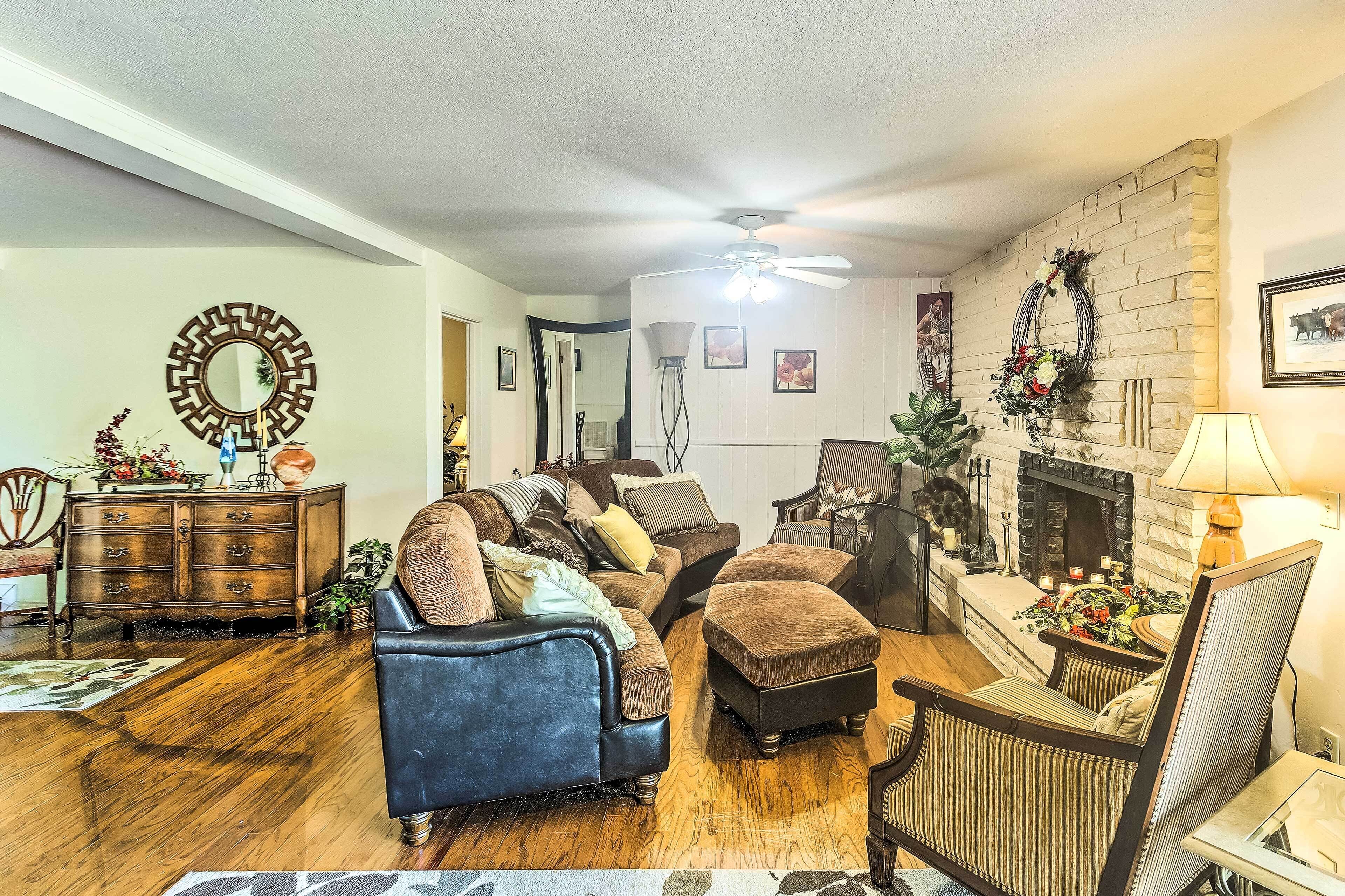 A cozy living room with a fireplace, a ceiling fan, and a large mirror on the wall.