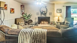 A cozy living room with a fireplace, comfortable seating, and a ceiling fan.