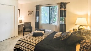 A bedroom with a bed, a chair, a desk, a window with curtains, and a lamp.