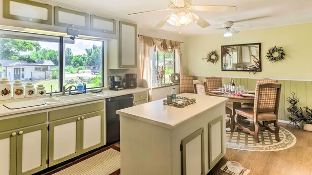 A kitchen with a central island, a dining area with a table and chairs, a ceiling fan, and a window with curtains.