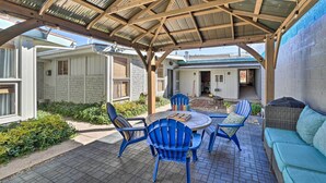 Un'area patio coperta con una pergola in legno, sedie blu, un tavolo rotondo e un divano verde.