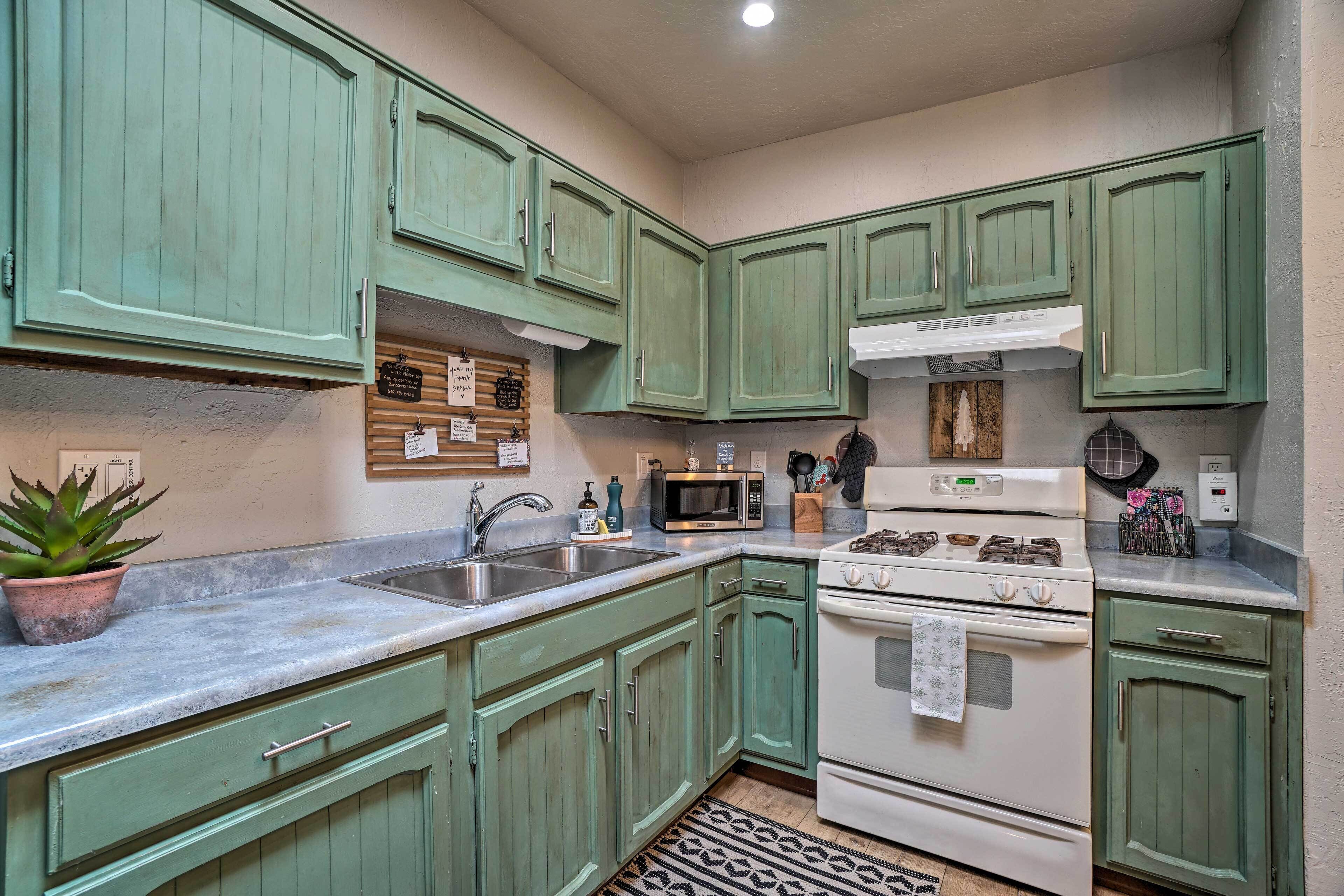 A kitchen with green cabinets, a white stove, a microwave, and a sink.