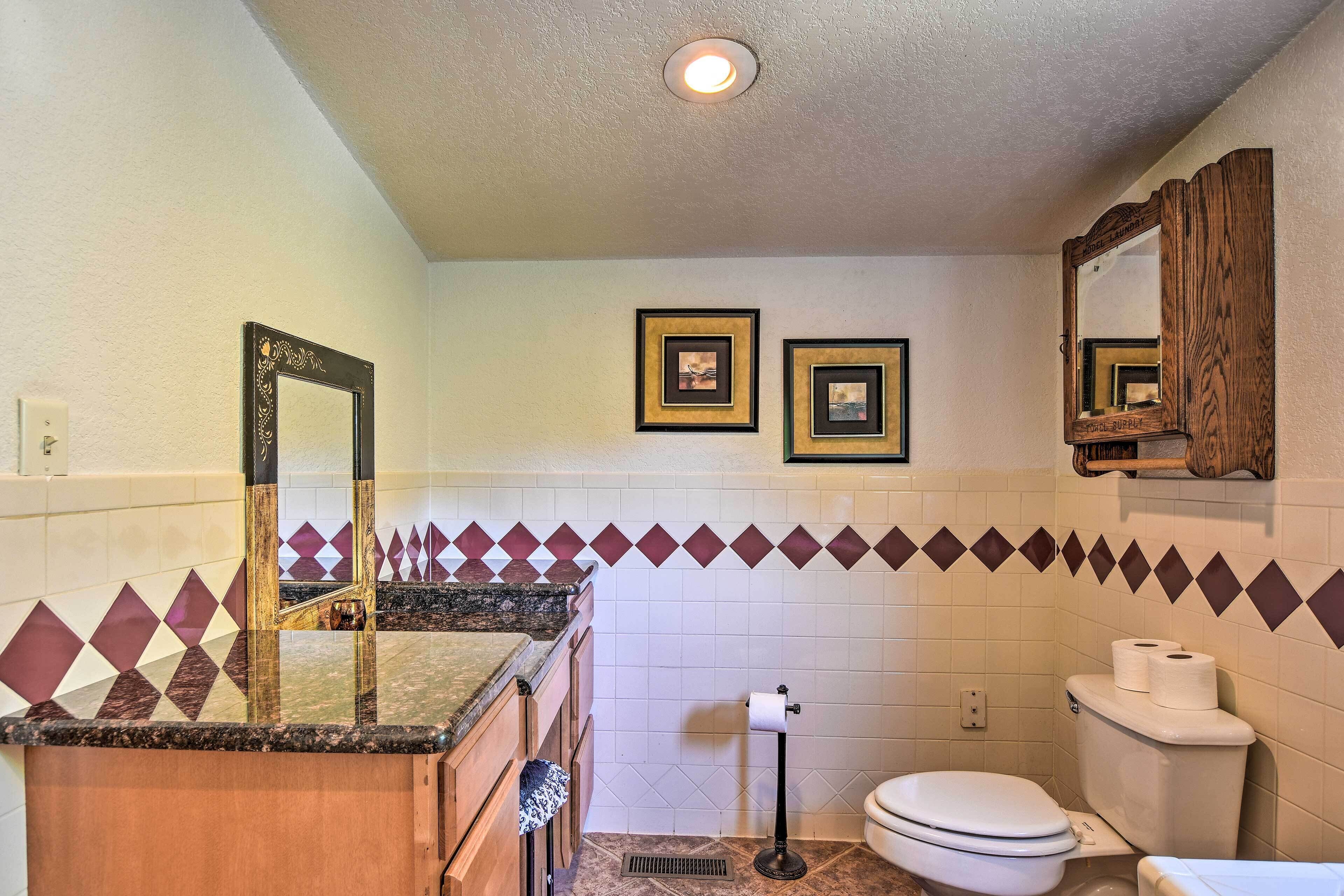 A bathroom with a sink, mirror, toilet, and two framed pictures on the wall.