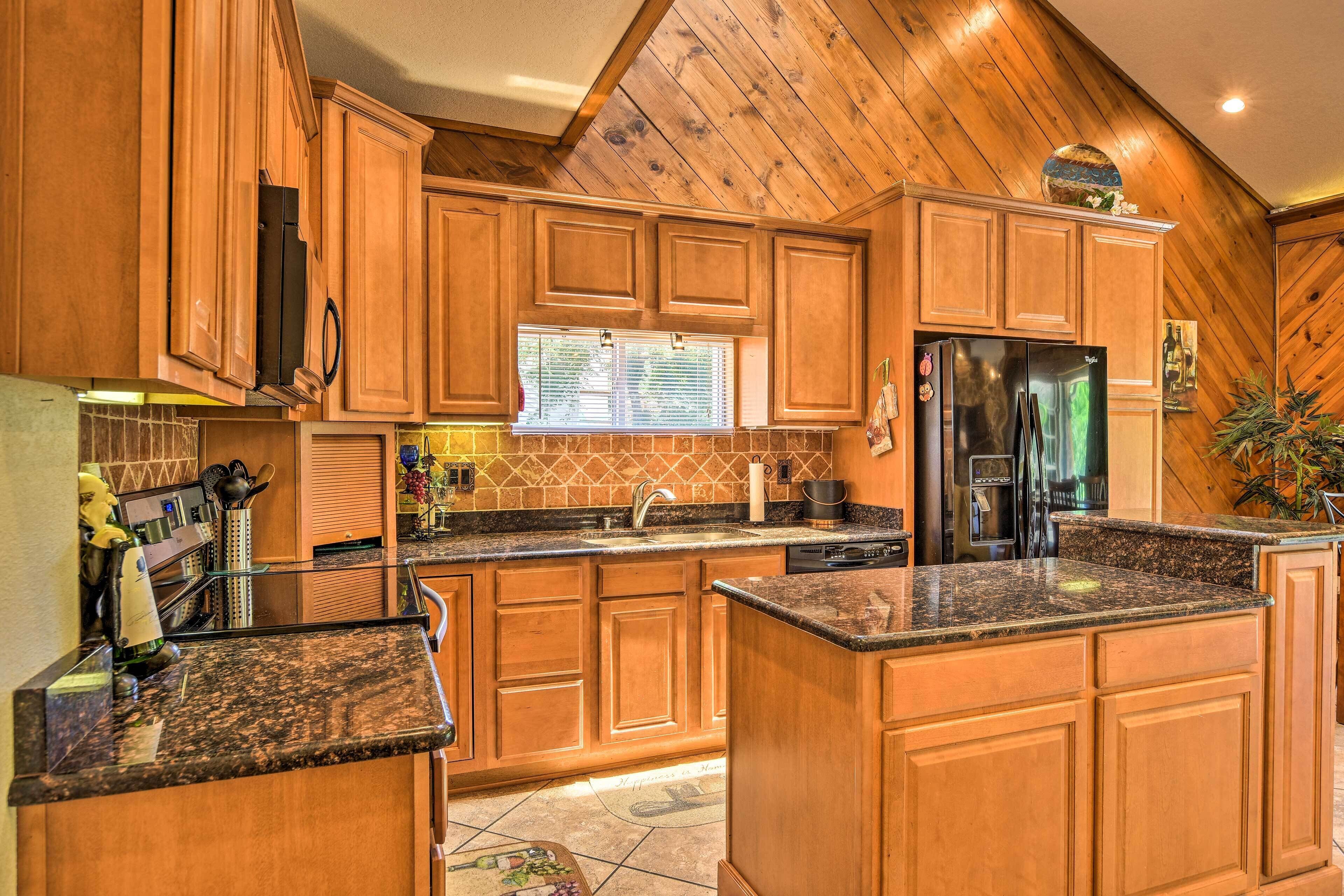 A kitchen with wooden cabinets, granite countertops, a refrigerator, and a window.
