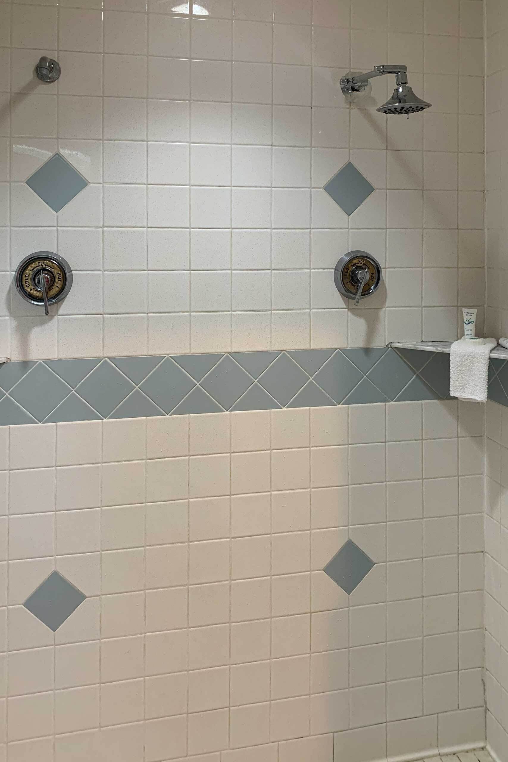 Une salle de bain avec des carreaux blancs, une pomme de douche et un porte-serviettes.