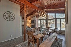 A dining area with a wooden table set for four, a large window with a view of trees, and a rustic ceiling with exposed beams. - Seneca Falls Cottage on Cayuga Lake Wine Trail! (Seneca Falls)