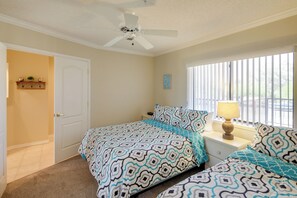 Un dormitorio con cama, mesita de noche, lámpara, ventilador de techo, ventana con persianas y puerta.