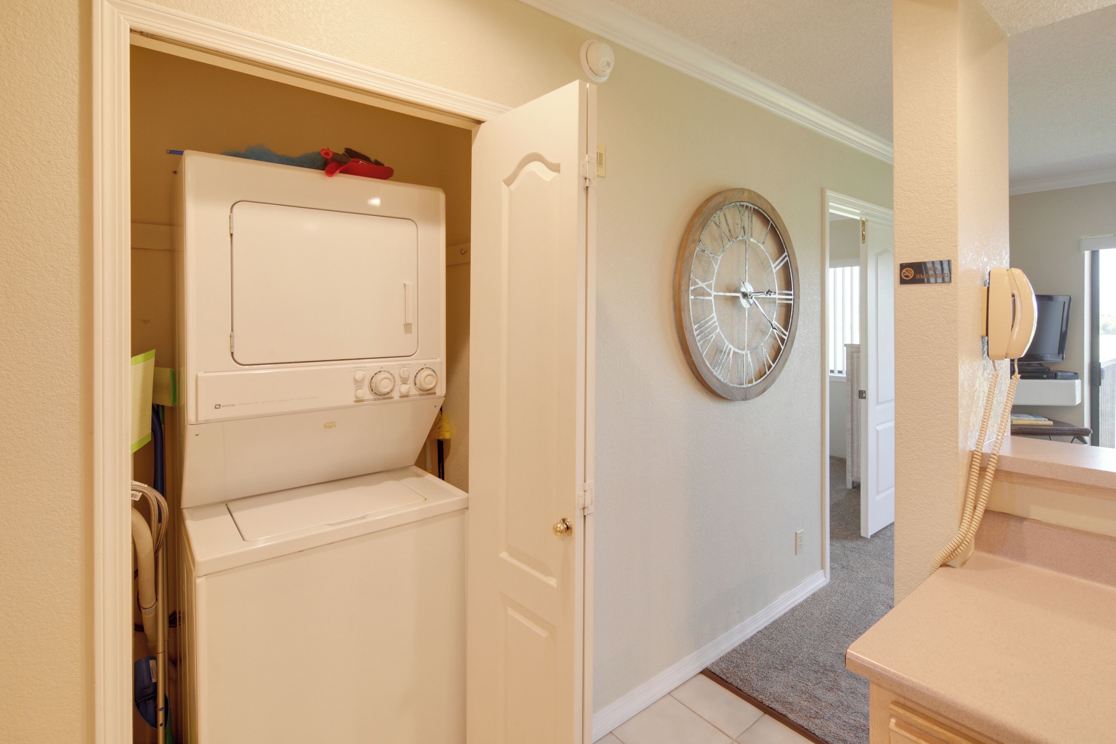 Une buanderie avec un lave-linge et un sèche-linge blancs, une horloge au mur et un téléphone.