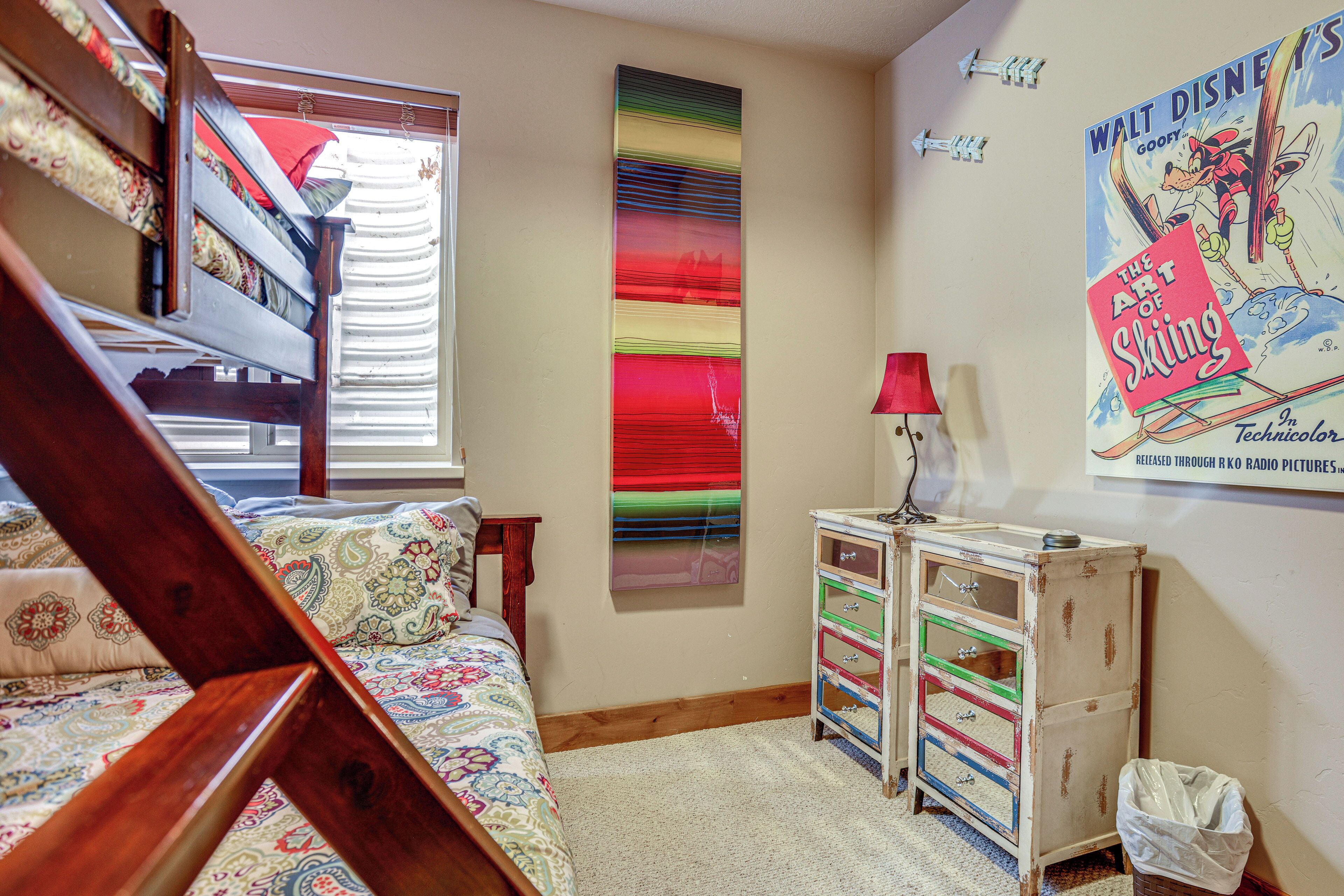 A bedroom with a bunk bed, a colorful striped wall, a poster of Walt Disney's 'The Art of Skiing', and a small dresser with drawers.