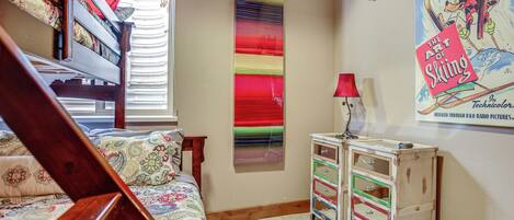 A bedroom with a bunk bed, a colorful striped wall, a poster of Walt Disney's 'The Art of Skiing', and a small dresser with drawers.