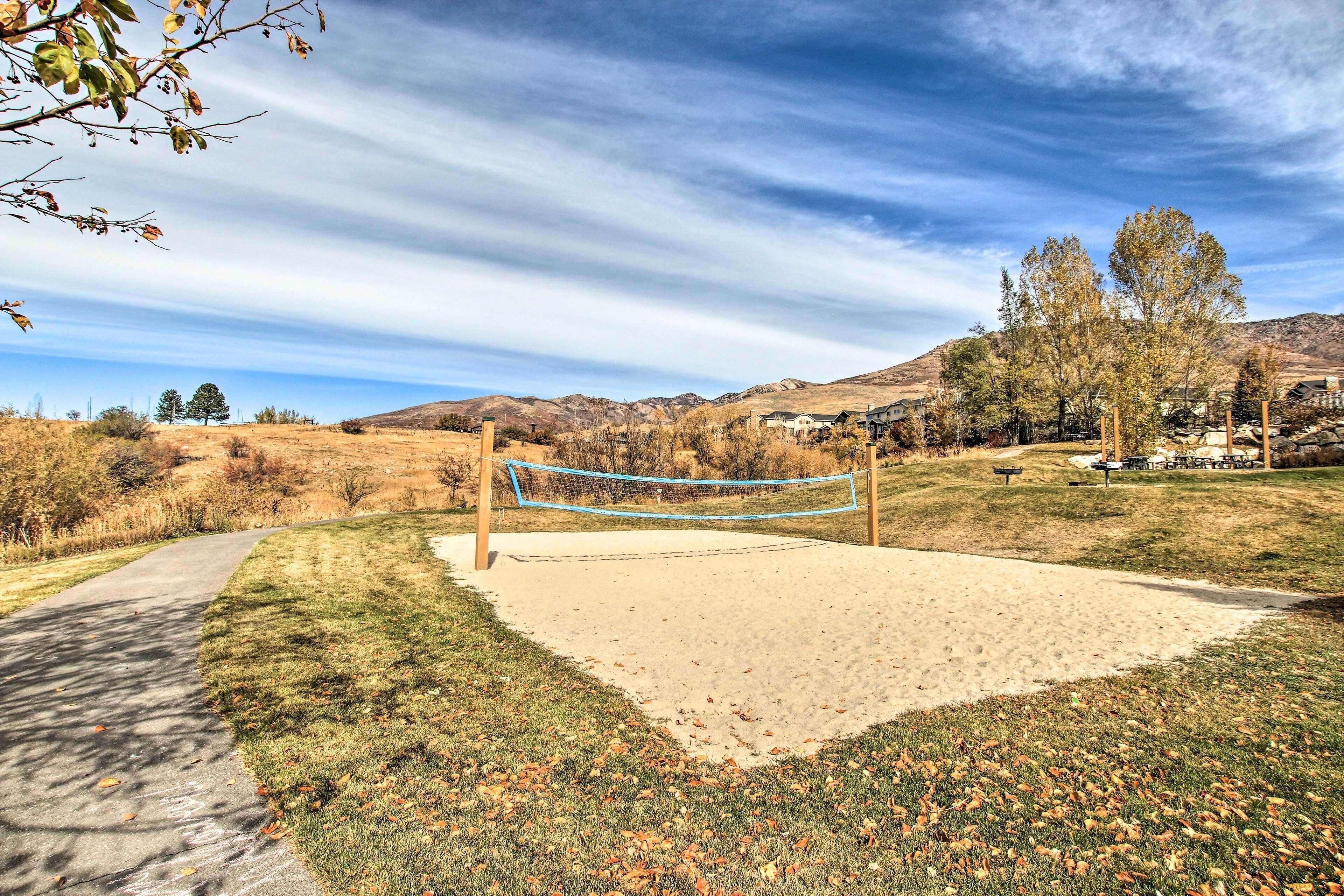 A volleyball net in a park with a paved path and grassy areas.