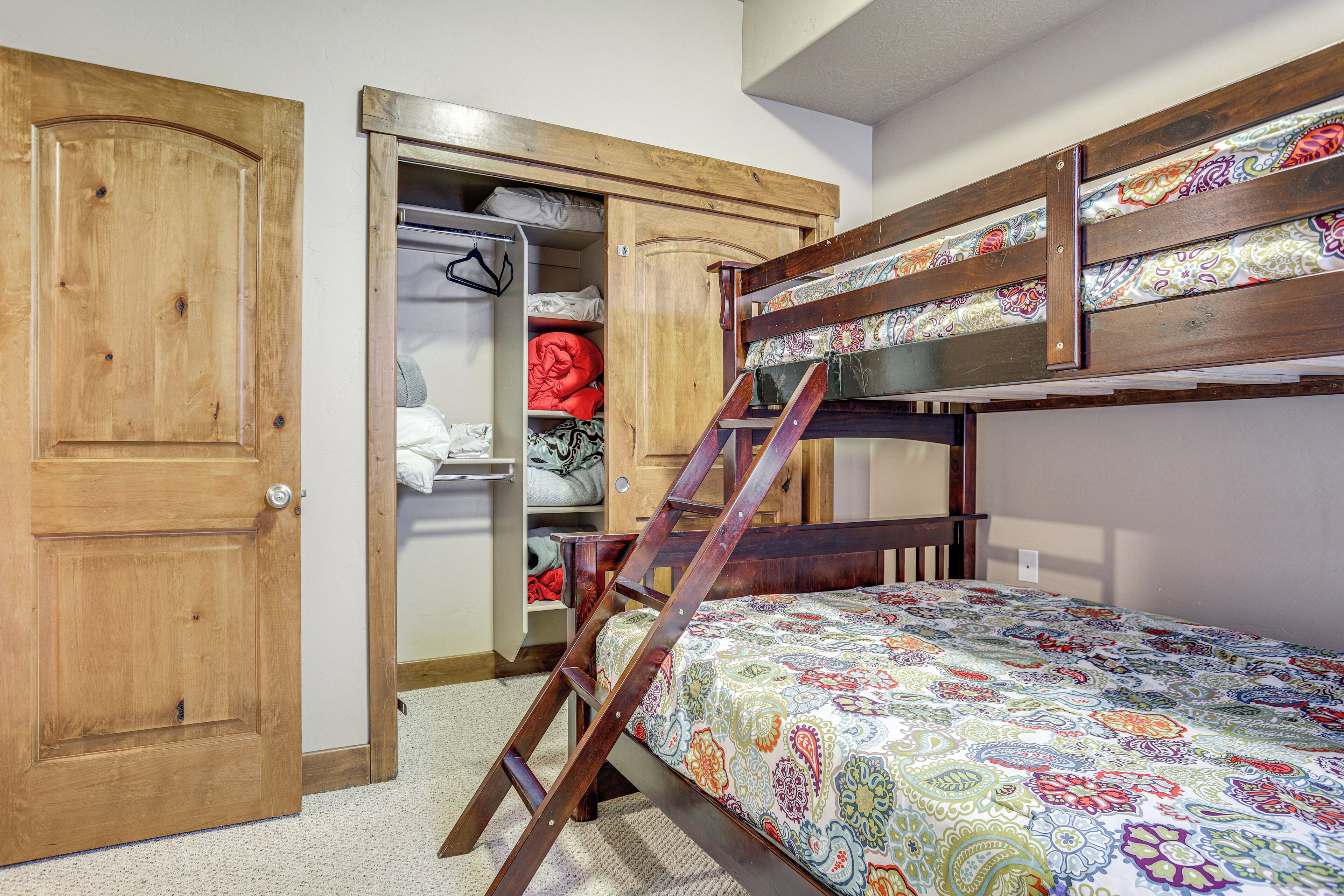 A room with a bunk bed, wooden wardrobe, and a closet with hanging clothes.