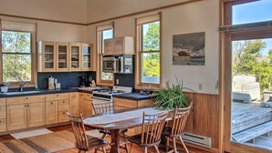 A modern kitchen with wooden cabinets, a central island, and a dining area with chairs. - Converted Historic Schoolhouse w/ Views! (Greybull)