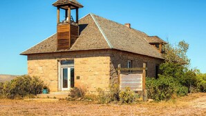 A stone building with a wooden tower, a door, and a signboard. - Converted Historic Schoolhouse w/ Views! (Greybull)