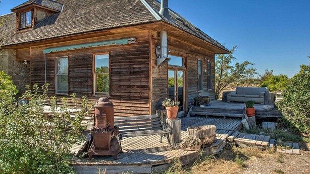 A rustic wooden cabin with a porch, a chimney, and a deck area. - Converted Historic Schoolhouse w/ Views! (Greybull)