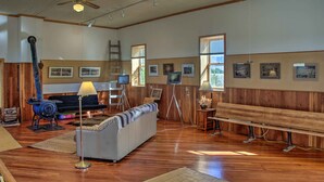 A spacious room with wooden floors, a sofa, a bench, and framed pictures on the walls. - Converted Historic Schoolhouse w/ Views! (Greybull)