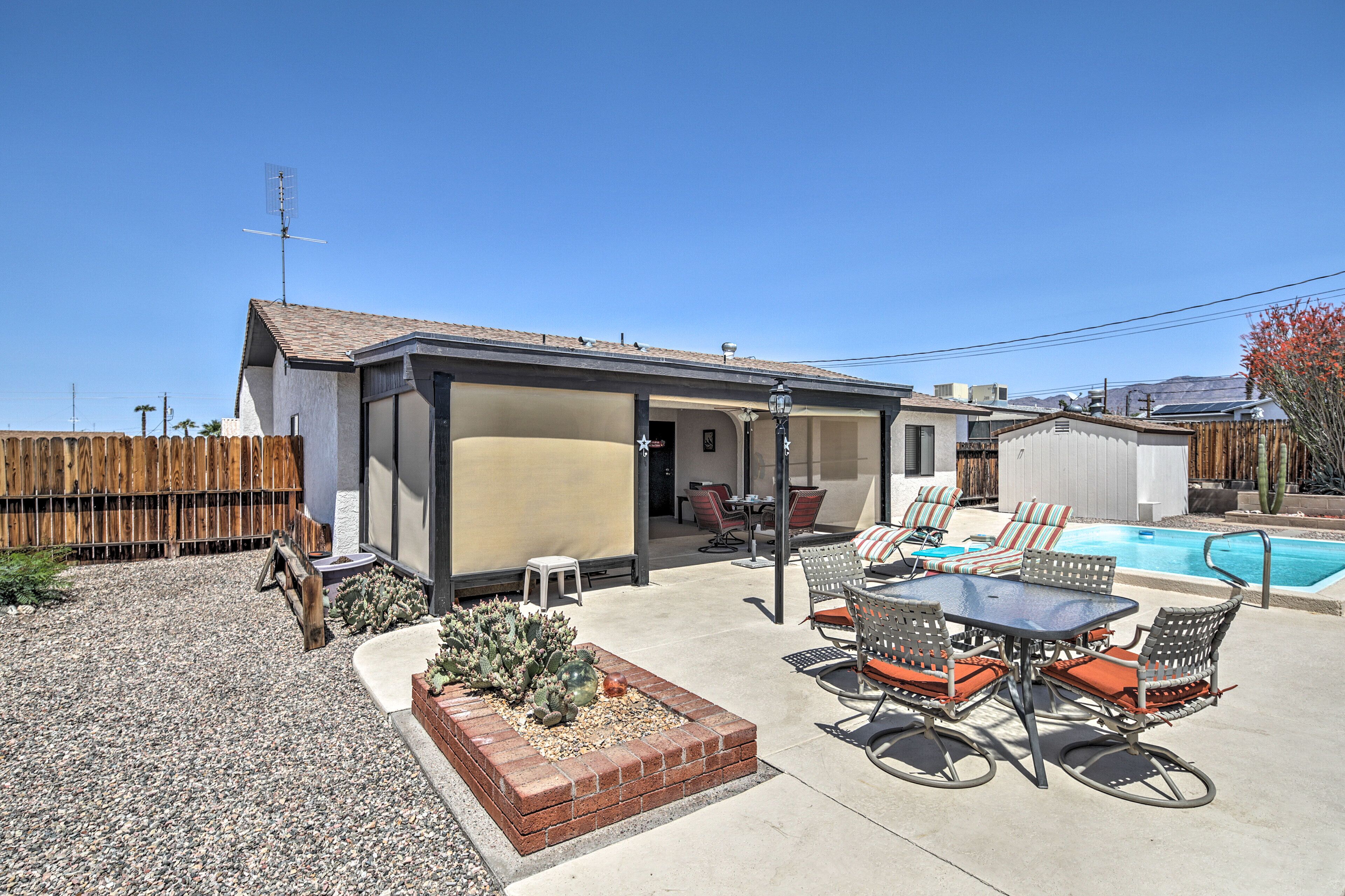 Un patio trasero con piscina, mobiliario de exterior y una pequeña construcción.