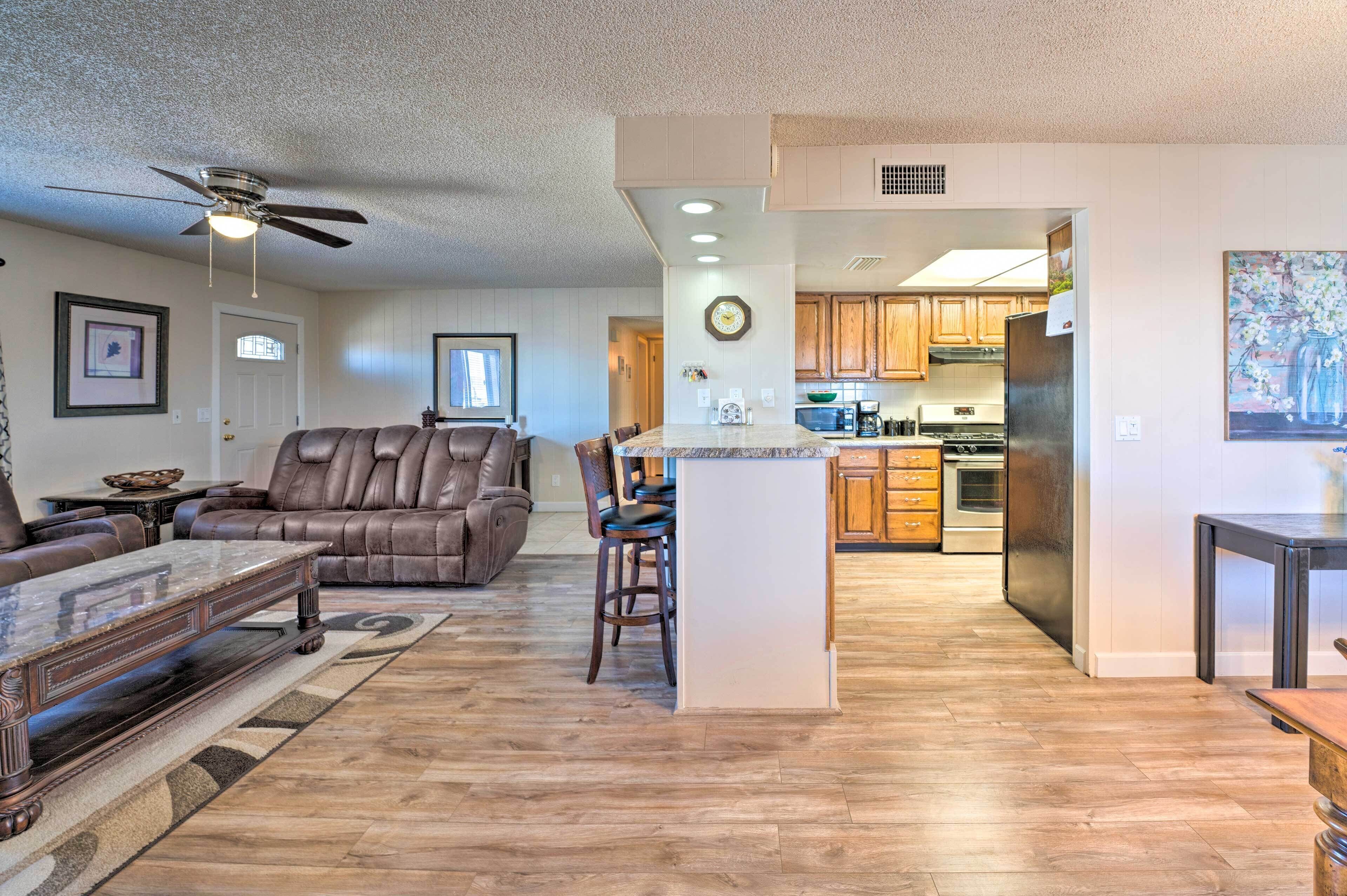 A spacious living room with a leather sofa, a coffee table, and a dining area with a kitchen in the background.