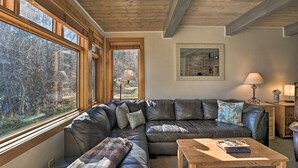 A cozy living room with a sectional sofa, a wooden coffee table, and a large window offering a view of trees. - Pool + Hot Tub Access! Ski Lovers Studio (Snowmass Village)