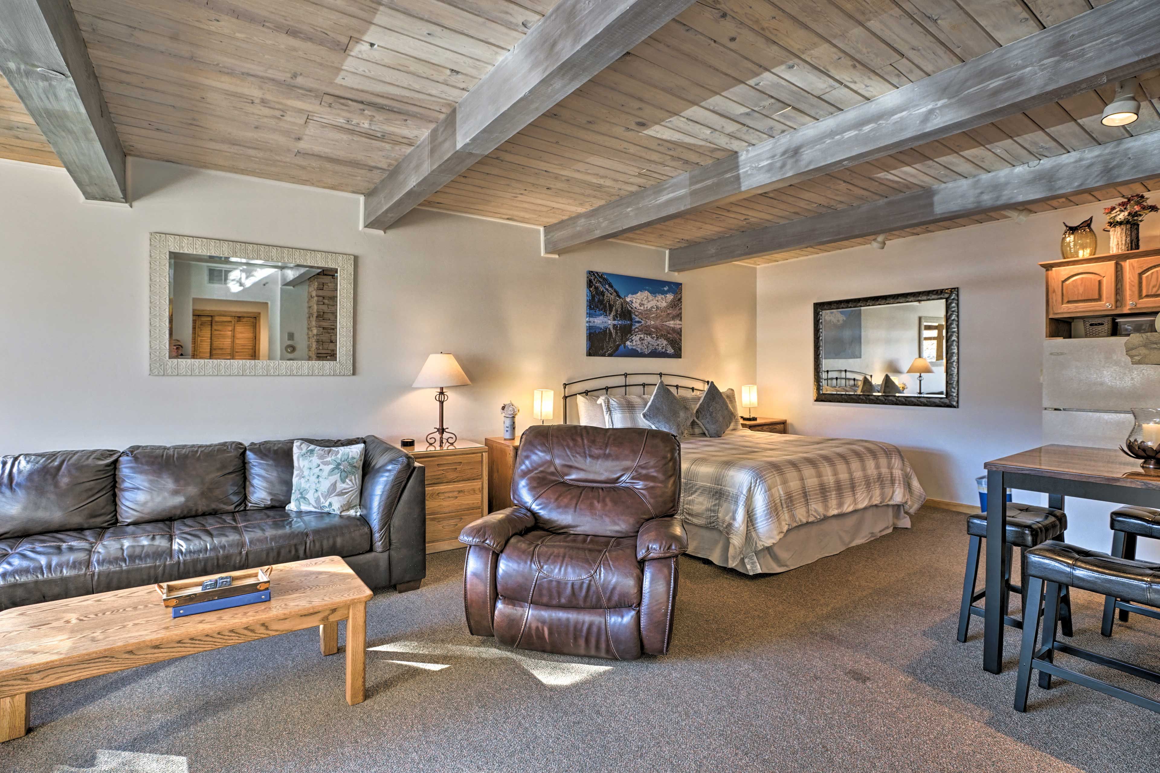 A cozy room with a leather sofa, a recliner, a bed, a dining table, and a mirror.