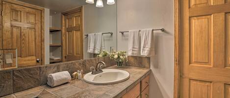 A bathroom with a marble countertop, wooden cabinets, a large mirror, and a towel rack.