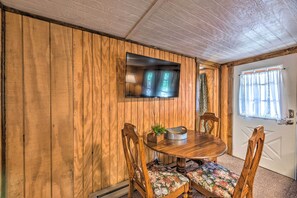 A wooden-paneled room with a round wooden table and two chairs, a mounted flat-screen TV, and a door with a window. - Pet-friendly Cloudcroft Cabin w/ Forest Views! (Cloudcroft)