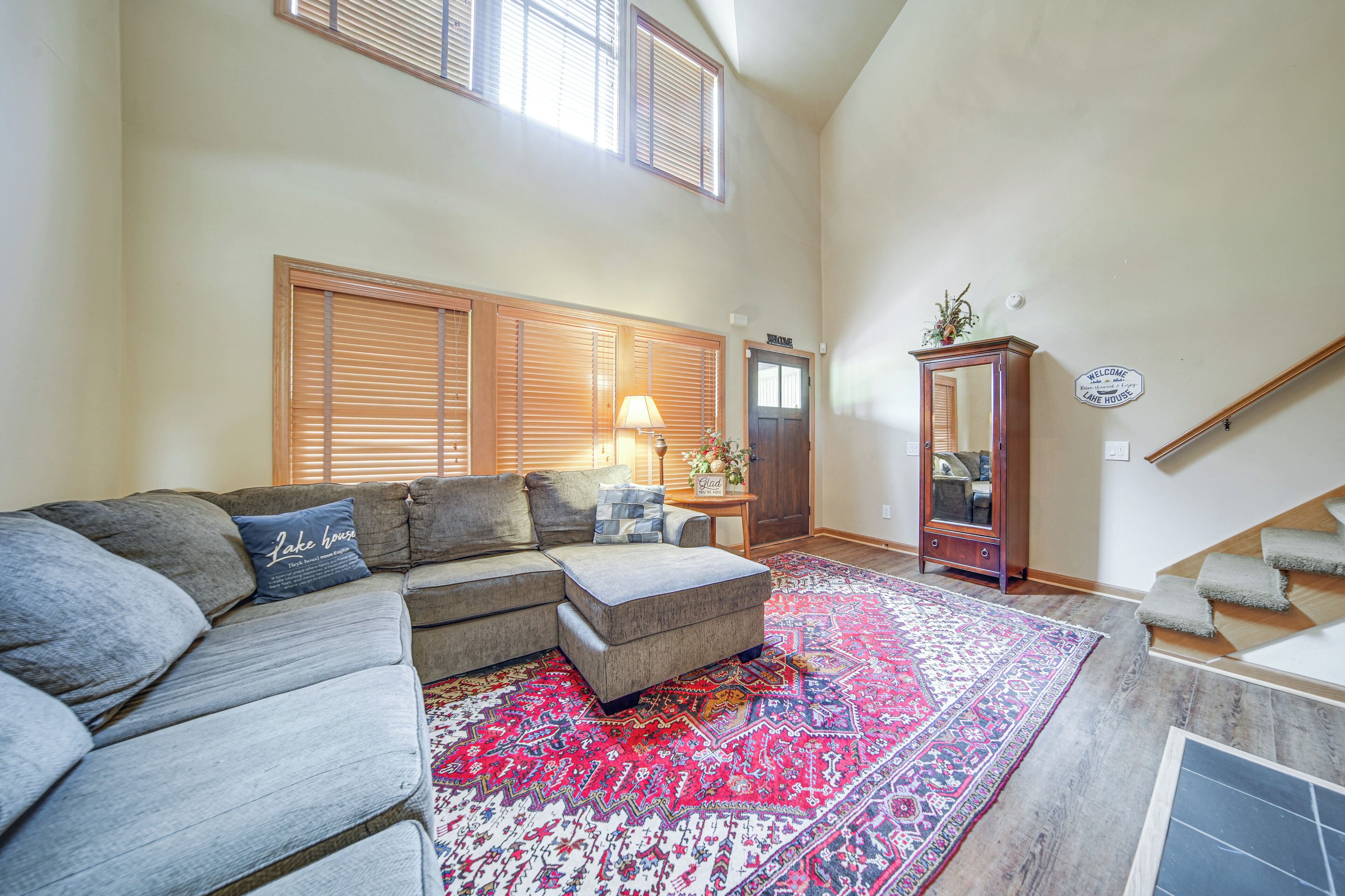 A living room with a sectional sofa, a patterned rug, a wooden cabinet, and a staircase.