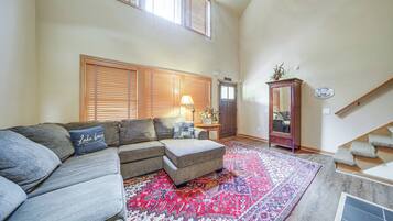A living room with a sectional sofa, a patterned rug, a wooden cabinet, and a staircase.